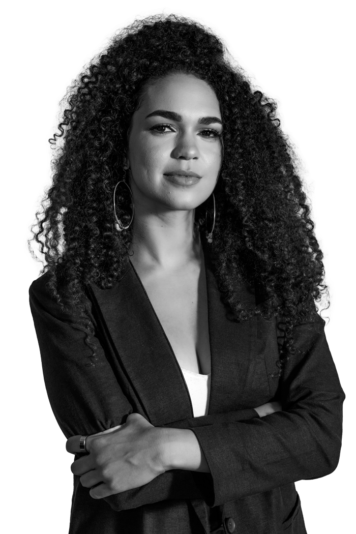 Sierra Stanton standing in a black blazer with her arms crossed. Sierra has long curly hair. She is looking directly at the